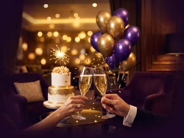 Un brindis junto a una torta y globos dorados y morados